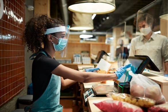 a cashier in protective gear rings up a customer at a grocery store