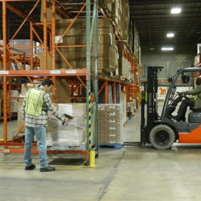 Warehouse with man scanning inventory and another operating a forklift