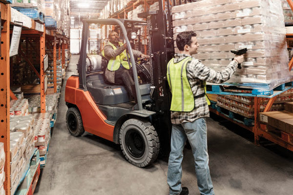Man using TOUGHBOOK handheld to scan pallet of cans lifted on a forklift