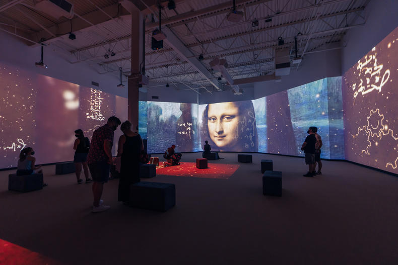 A group of on-lookers stand amidst immersive projections of Leonardo Da Vinci's works featuring Mona Lisa