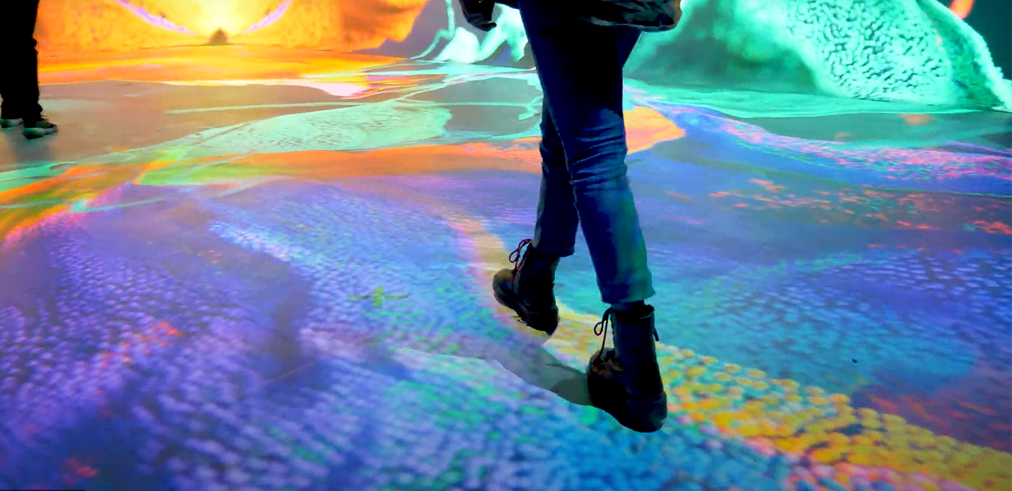 we see a person's legs as they move through an immersive exhibit space created by a series of projectors