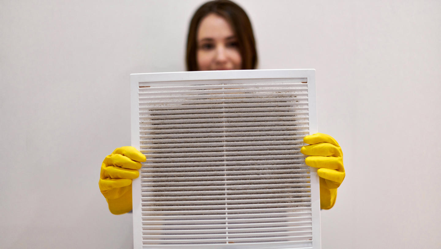 Woman holding dirty and dusty ventilation grille, blurred.