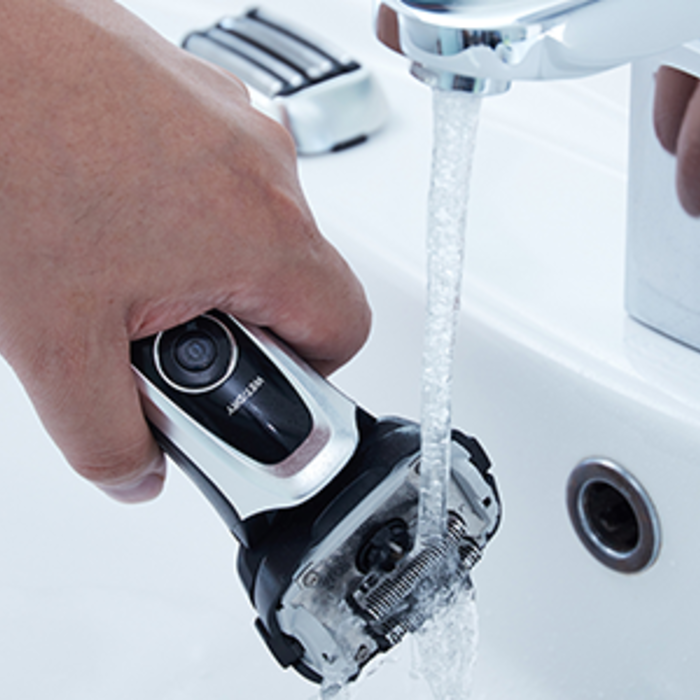 User's hand holding the ES-LV65-S shaver under running water. 