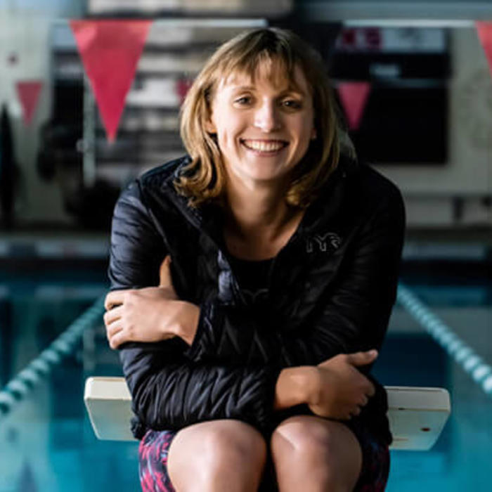 Katie Ledecky poses in front of an Olympic swimming pool