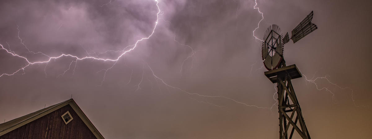 Anvil crawling lightning illuminates an old barn during a thunderstorm