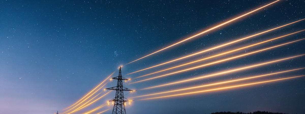 Electricity transmission towers with orange glowing wires against night sky.