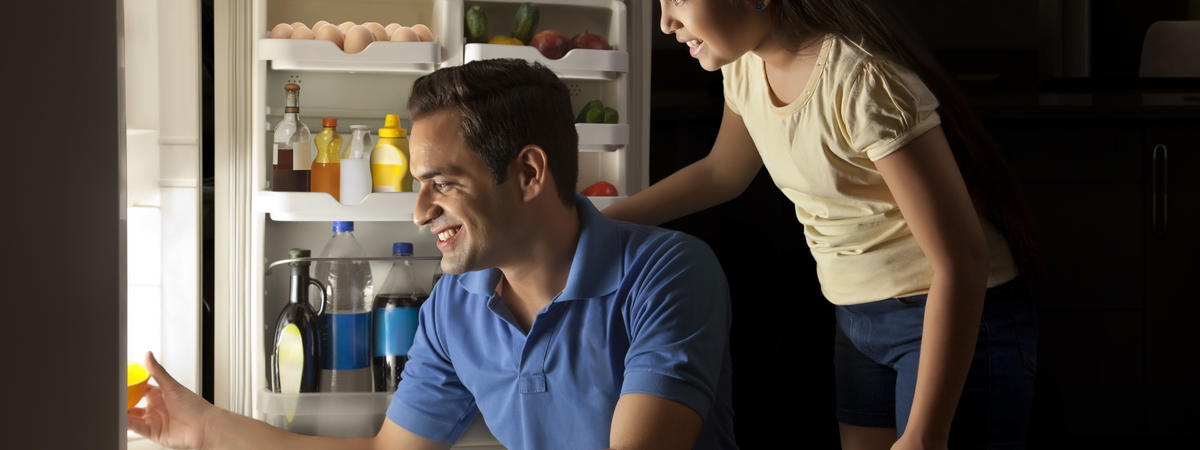 Father and daughter keeping food in refrigerator at night