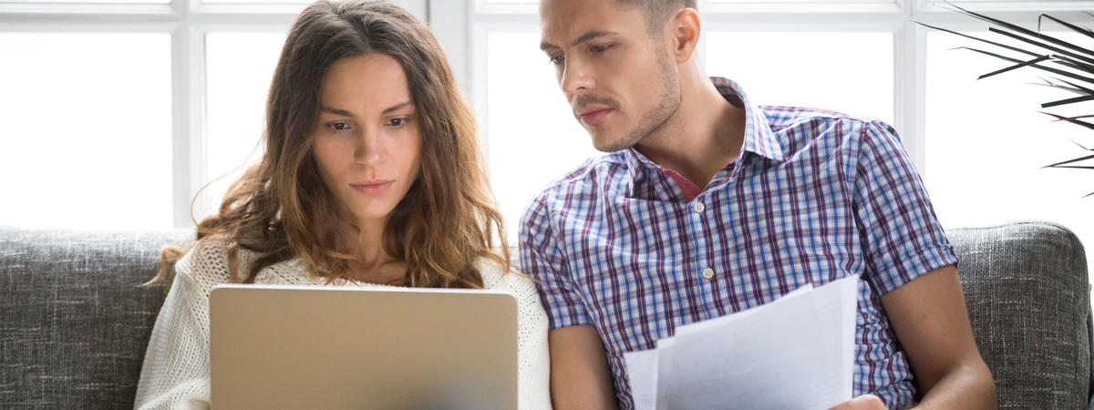 Focused worried couple paying bills online on laptop with documents