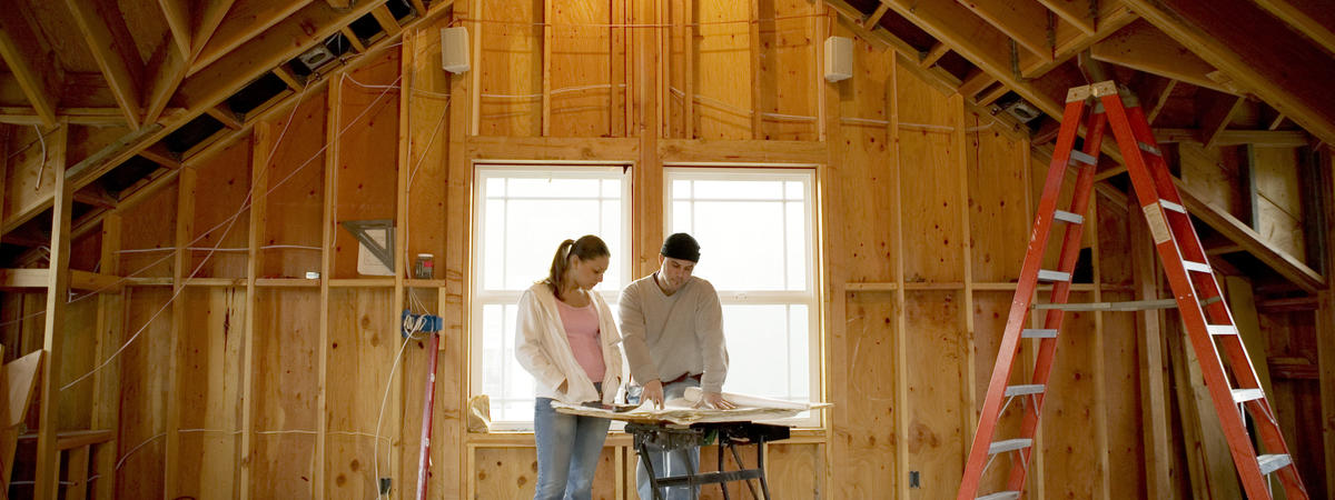 Man and young woman looking at blueprints in house under construction