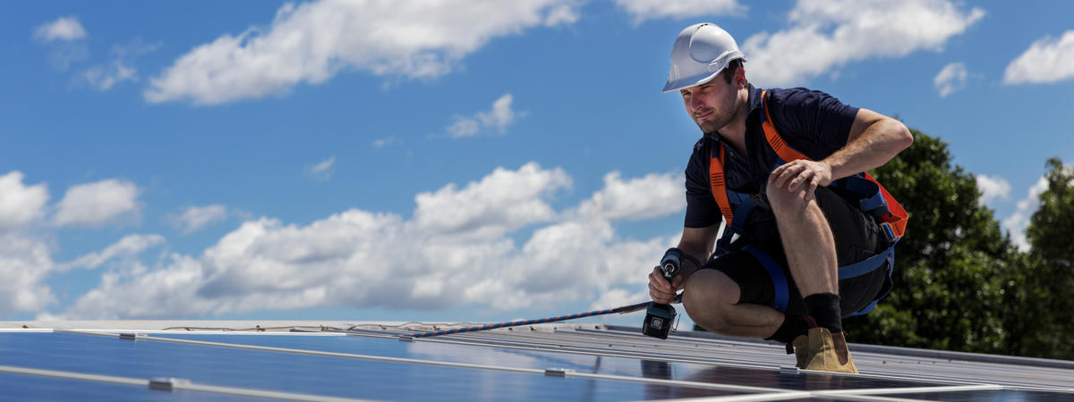 Technician with drill installing solar panels on roof