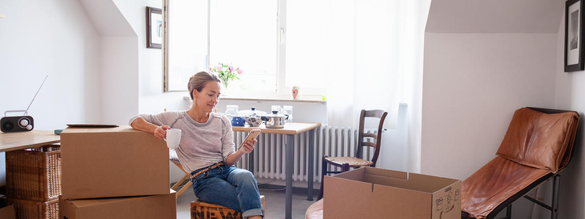 Woman taking a coffee break while moving house, text messaging on mobile phone