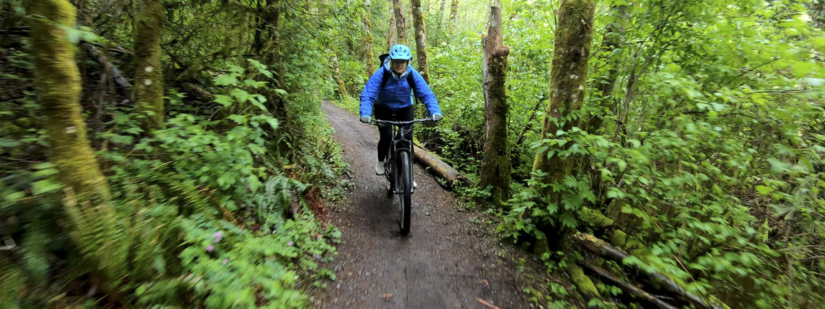 Woman mountain bikes down a narrow path through the forest in the rain