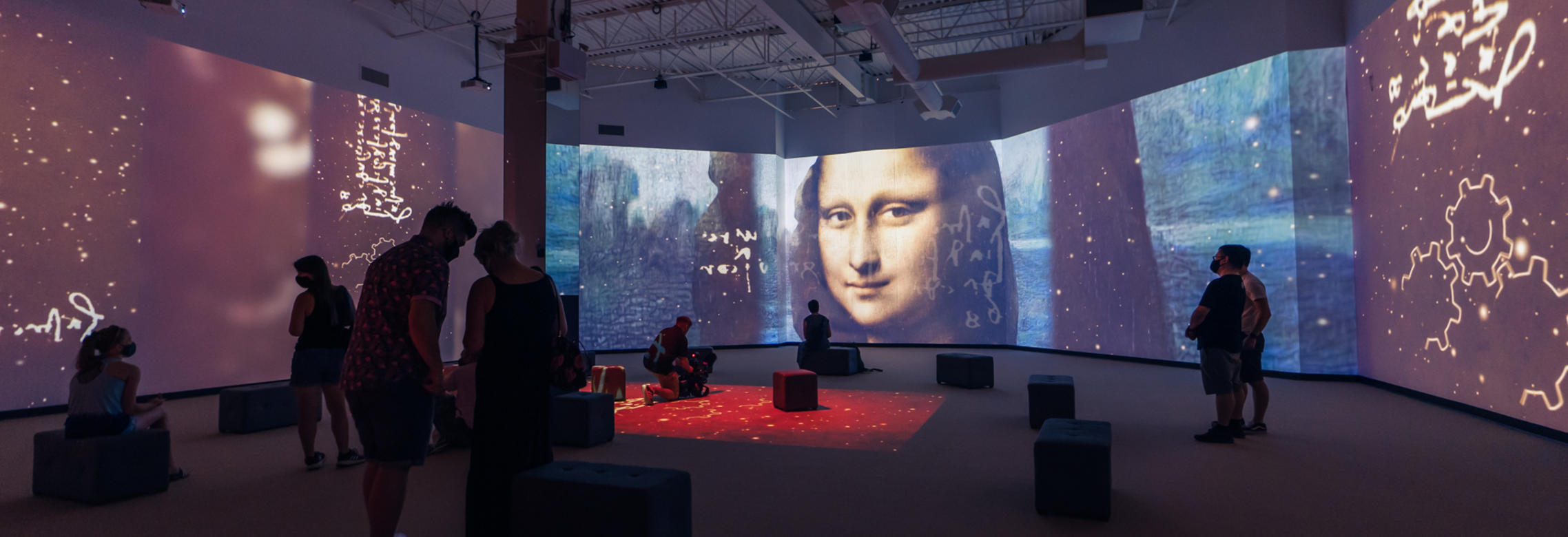 A group of on-lookers stand amidst immersive projections of Leonardo Da Vinci's works featuring Mona Lisa