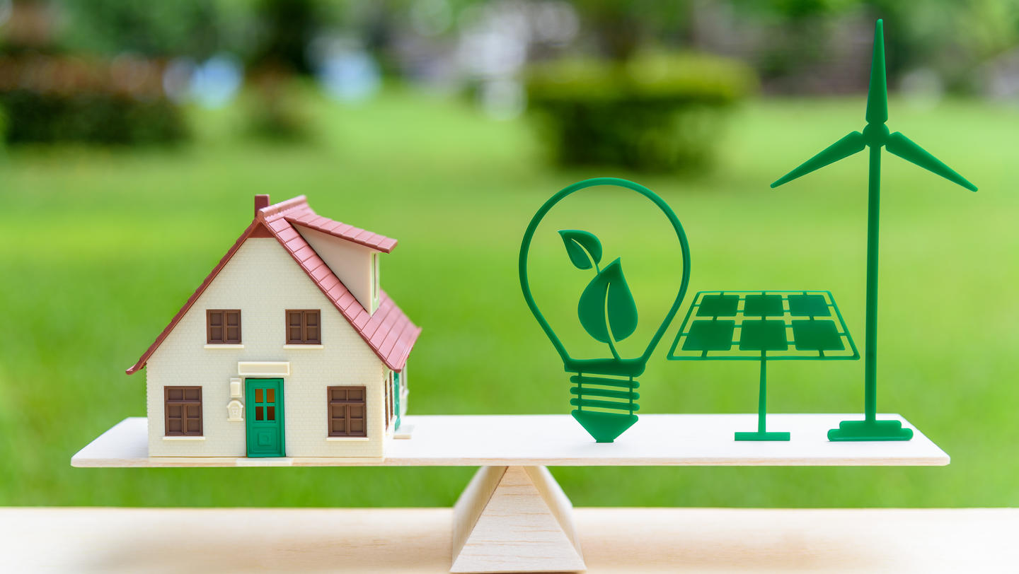Future clean / renewable or alternative energy for modern living concept : House model, light bulb with green leaf, solar panel, wind mill on wood balance scale, depicts the awareness of environment.